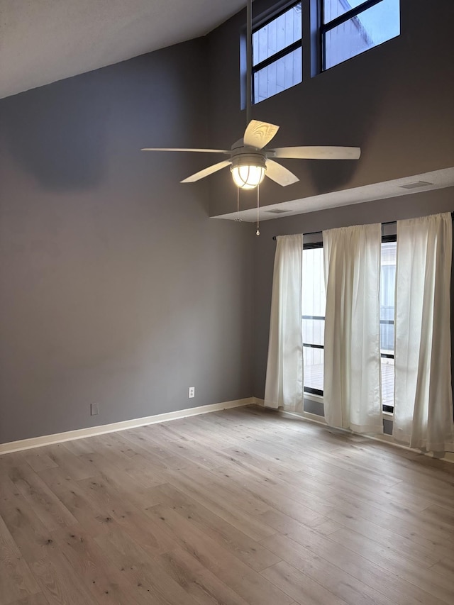 unfurnished room with ceiling fan, light wood-type flooring, and a towering ceiling