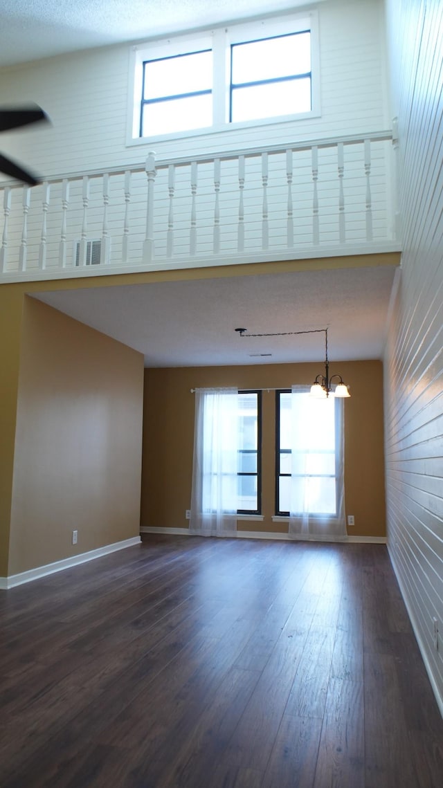 empty room featuring a towering ceiling, an inviting chandelier, and dark wood-type flooring