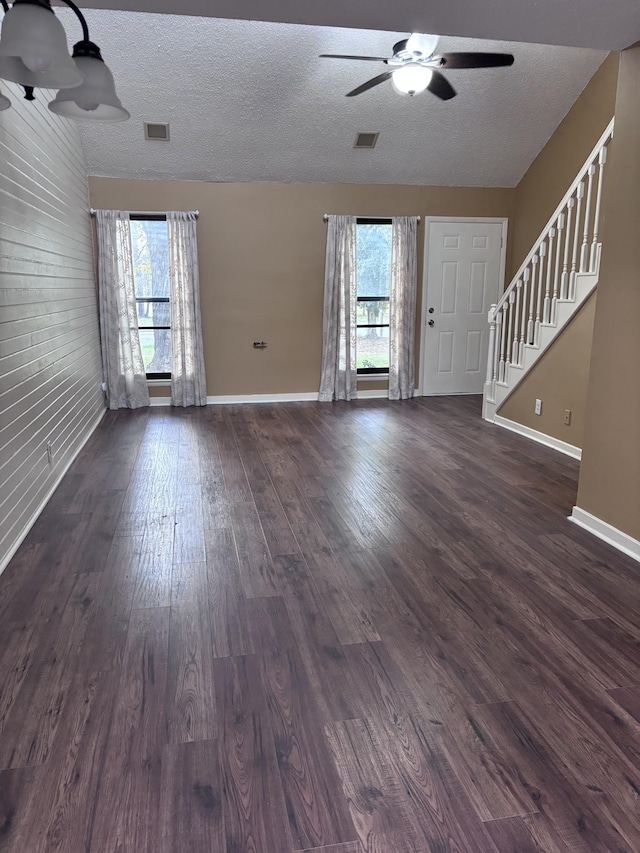 interior space with a textured ceiling, dark hardwood / wood-style flooring, ceiling fan, and wooden walls