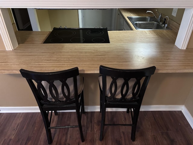 interior space with a kitchen bar, kitchen peninsula, sink, dark hardwood / wood-style floors, and black stovetop