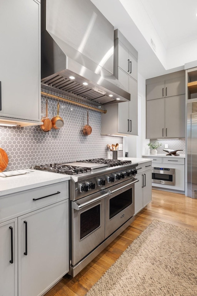 kitchen with backsplash, light hardwood / wood-style floors, wall chimney range hood, and high end appliances