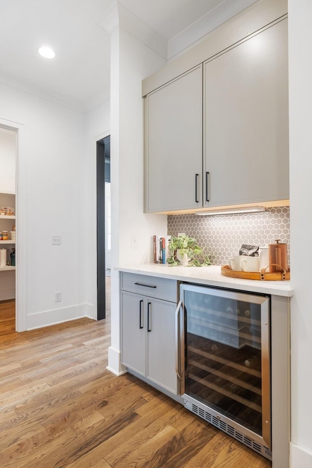 bar featuring beverage cooler, crown molding, light hardwood / wood-style floors, gray cabinets, and decorative backsplash