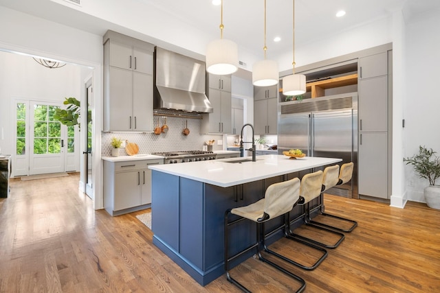 kitchen with sink, a center island with sink, gray cabinets, and wall chimney range hood