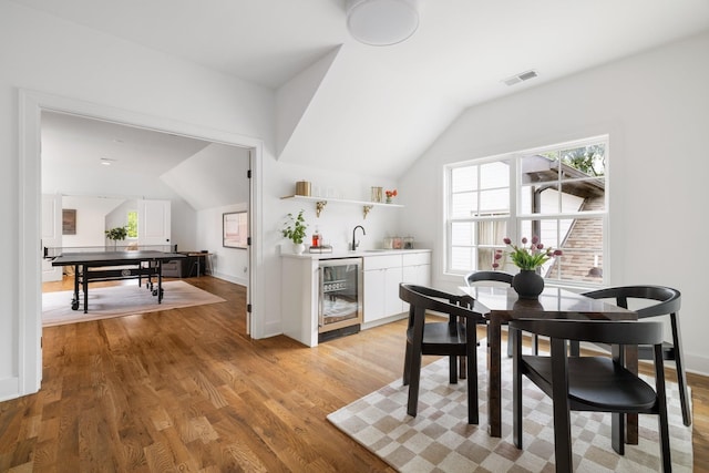 dining room with light wood-type flooring, wet bar, beverage cooler, and vaulted ceiling