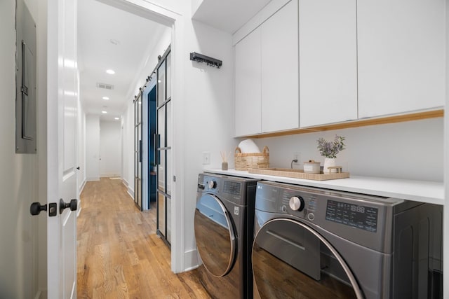 washroom featuring washer and dryer, a barn door, cabinets, and light wood-type flooring