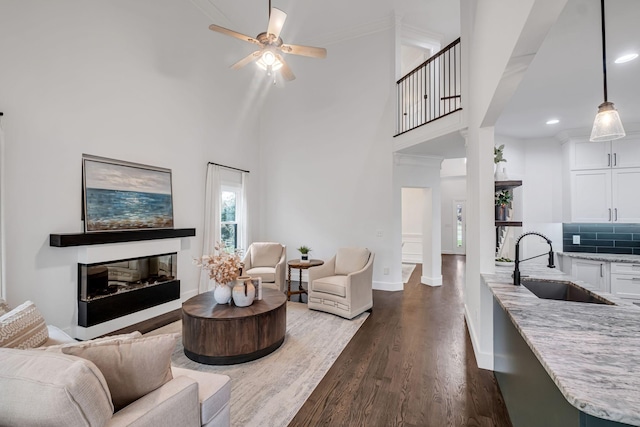 living room with a towering ceiling, dark hardwood / wood-style flooring, ornate columns, ceiling fan, and sink