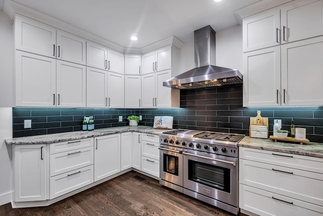 kitchen with decorative backsplash, dark wood-type flooring, wall chimney range hood, double oven range, and white cabinetry