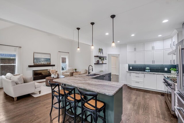 kitchen with light stone counters, a breakfast bar, stainless steel stove, white cabinetry, and hanging light fixtures