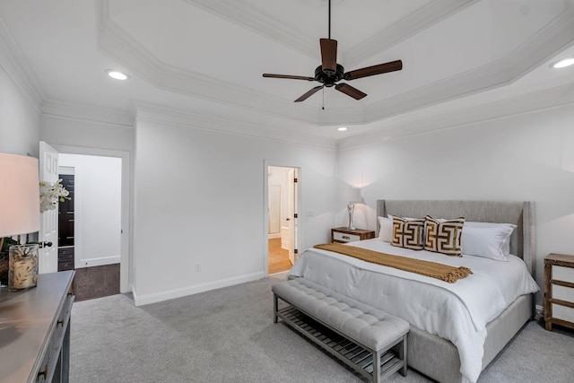 bedroom featuring light carpet, ensuite bath, a tray ceiling, ceiling fan, and crown molding