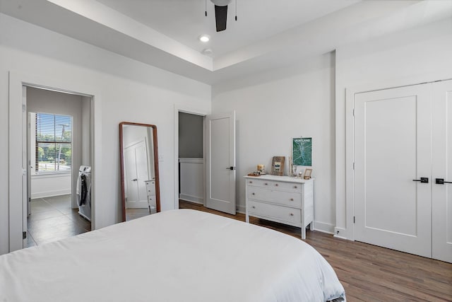 bedroom with ceiling fan, independent washer and dryer, dark wood-type flooring, and a tray ceiling