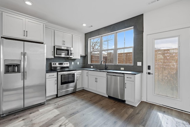 kitchen with appliances with stainless steel finishes, light wood-type flooring, tasteful backsplash, sink, and white cabinets