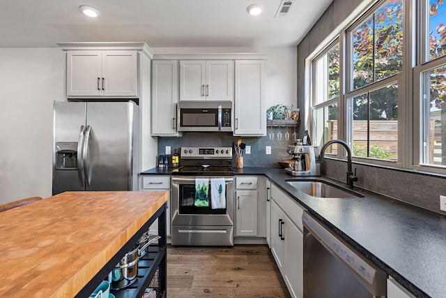 kitchen with appliances with stainless steel finishes, dark wood-type flooring, sink, butcher block countertops, and white cabinetry