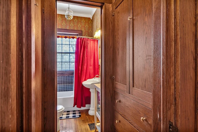 bathroom with ornamental molding, wood-type flooring, shower / tub combo, and toilet