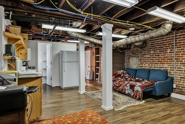 basement featuring hardwood / wood-style flooring, white fridge, and brick wall