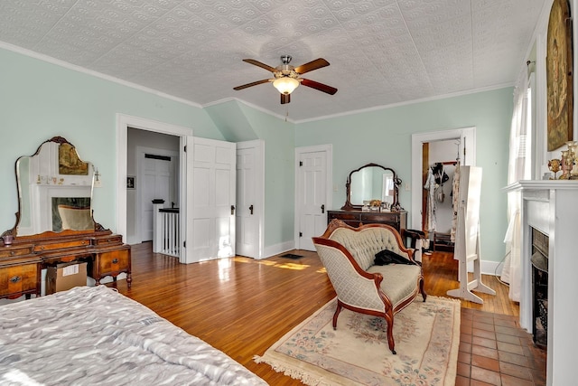 bedroom featuring hardwood / wood-style flooring, ceiling fan, ornamental molding, and a tile fireplace