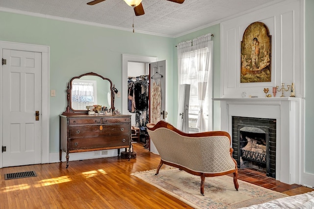 living area with a textured ceiling, hardwood / wood-style flooring, ceiling fan, and crown molding