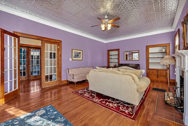 living room featuring built in shelves, ceiling fan, french doors, dark hardwood / wood-style floors, and crown molding