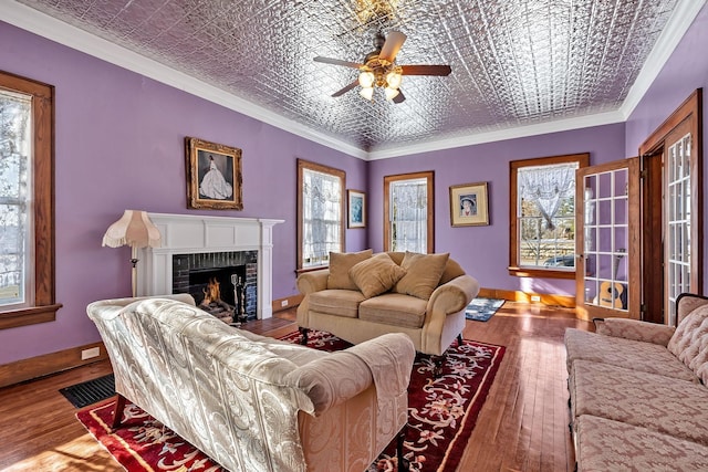 living room with crown molding, hardwood / wood-style flooring, ceiling fan, a fireplace, and a wealth of natural light