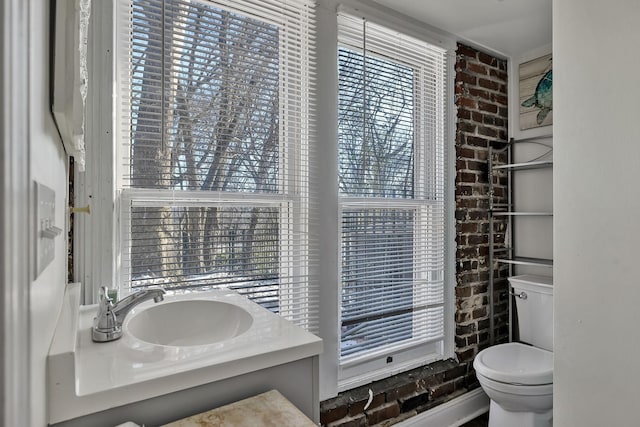 bathroom featuring sink, toilet, and brick wall