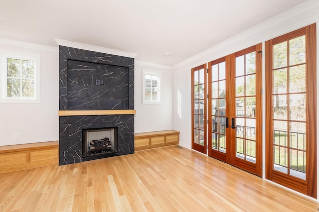 unfurnished living room featuring a wealth of natural light, hardwood / wood-style floors, a fireplace, ornamental molding, and french doors