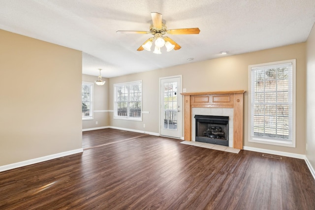 unfurnished living room with ceiling fan, dark hardwood / wood-style flooring, a textured ceiling, and a tile fireplace