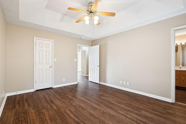 unfurnished bedroom with dark hardwood / wood-style flooring, connected bathroom, a tray ceiling, and ceiling fan