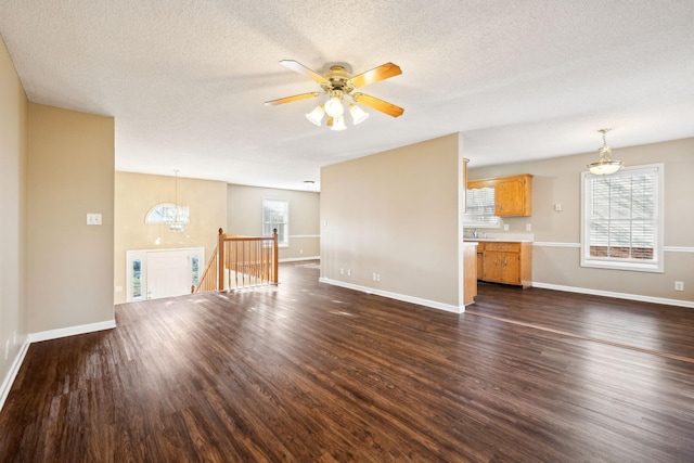 unfurnished living room featuring a textured ceiling, sink, dark wood-type flooring, and ceiling fan with notable chandelier