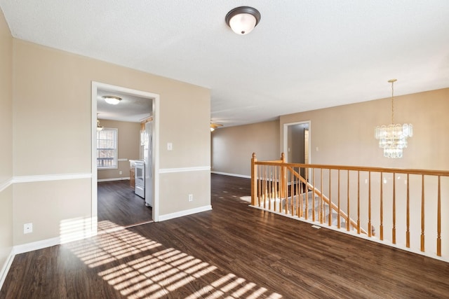 unfurnished room with dark wood-type flooring, a textured ceiling, and an inviting chandelier