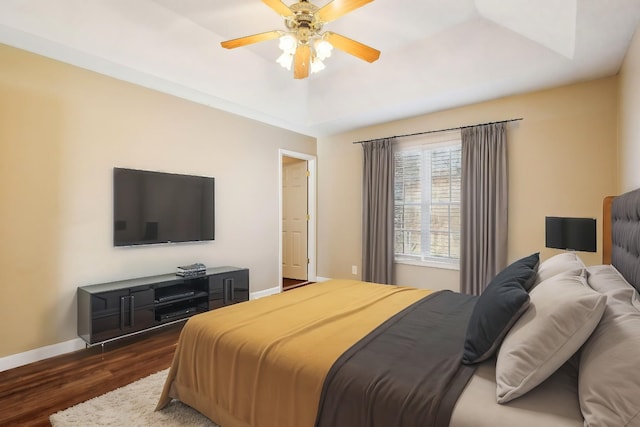 bedroom with ceiling fan, dark hardwood / wood-style flooring, and a tray ceiling