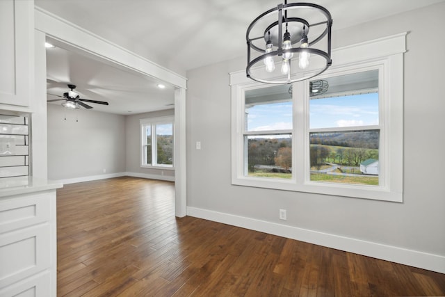 unfurnished dining area with dark hardwood / wood-style floors and ceiling fan with notable chandelier