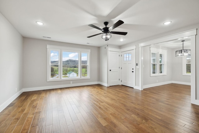 unfurnished living room featuring ceiling fan with notable chandelier and wood-type flooring