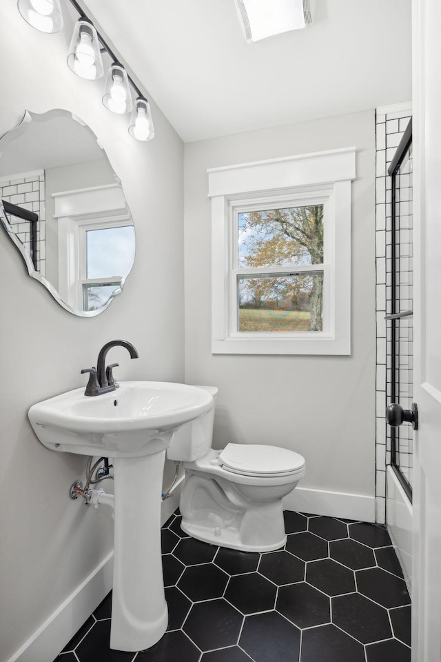 bathroom with toilet, a healthy amount of sunlight, and enclosed tub / shower combo