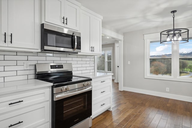 kitchen featuring dark wood-type flooring, backsplash, an inviting chandelier, appliances with stainless steel finishes, and white cabinetry