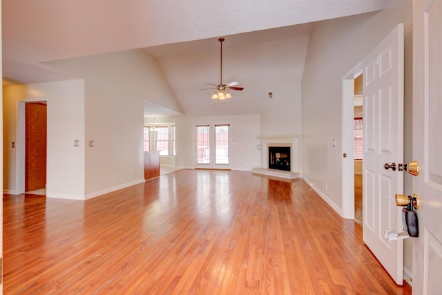 unfurnished living room featuring baseboards, a fireplace with raised hearth, ceiling fan, and light wood finished floors