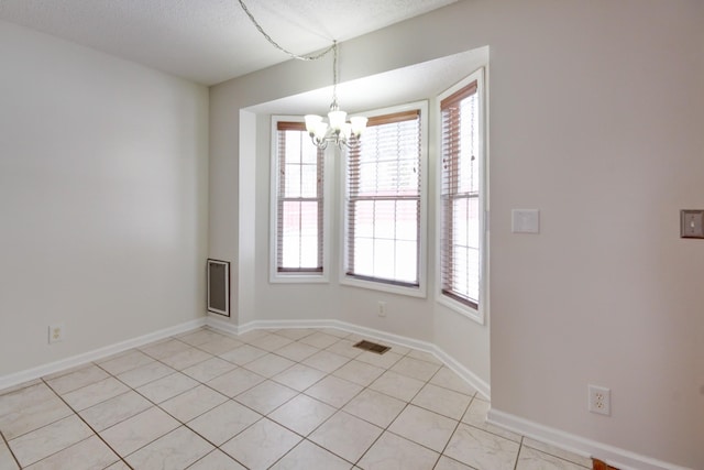 spare room featuring a notable chandelier, visible vents, baseboards, and a textured ceiling