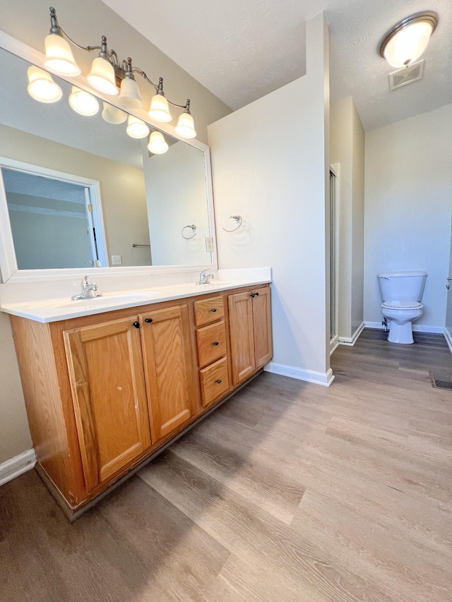 bathroom featuring vanity, a textured ceiling, a shower with door, wood-type flooring, and toilet