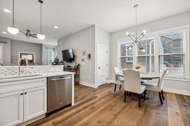 kitchen with stainless steel dishwasher, sink, pendant lighting, wood-type flooring, and white cabinets