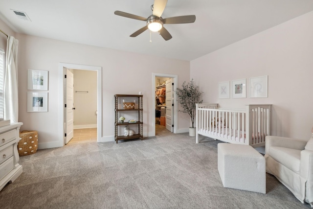 carpeted bedroom featuring ceiling fan, a spacious closet, connected bathroom, a crib, and a closet