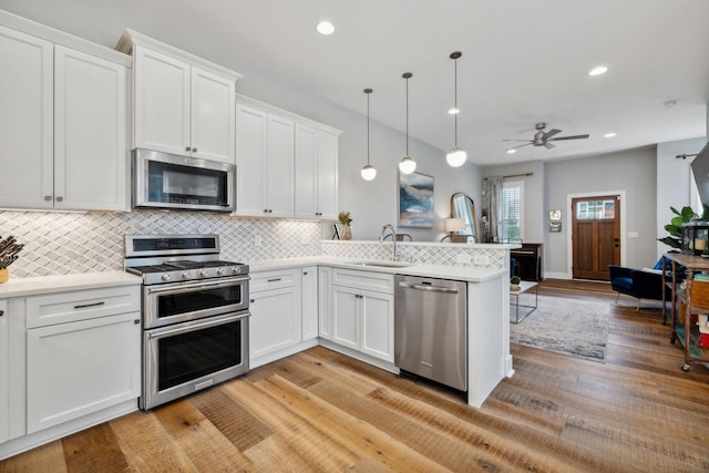 kitchen with decorative light fixtures, white cabinetry, kitchen peninsula, and appliances with stainless steel finishes