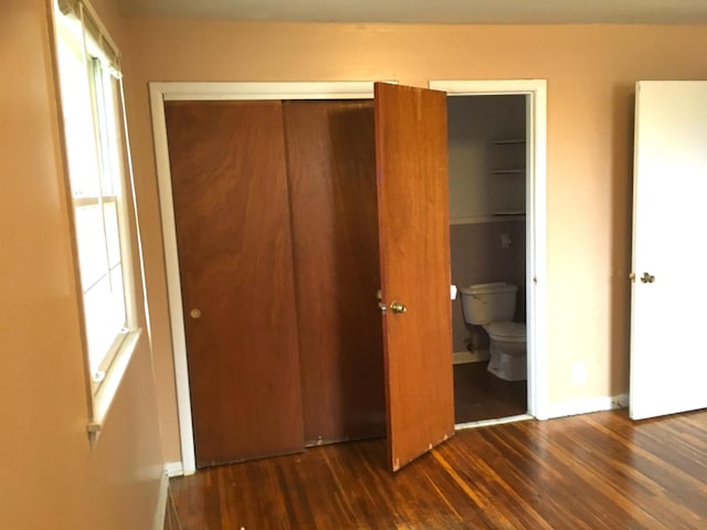 unfurnished bedroom with dark hardwood / wood-style flooring, multiple windows, connected bathroom, and a closet