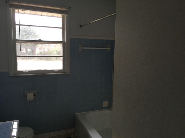 bathroom with bathing tub / shower combination, toilet, and tile walls