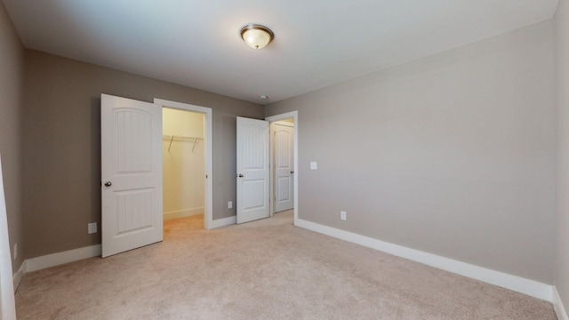 unfurnished bedroom featuring a walk in closet, a closet, and light colored carpet