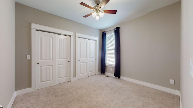 unfurnished bedroom with multiple closets, ceiling fan, and light carpet