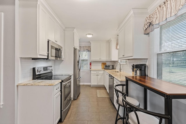 kitchen featuring white cabinets, light stone countertops, stainless steel appliances, and tasteful backsplash