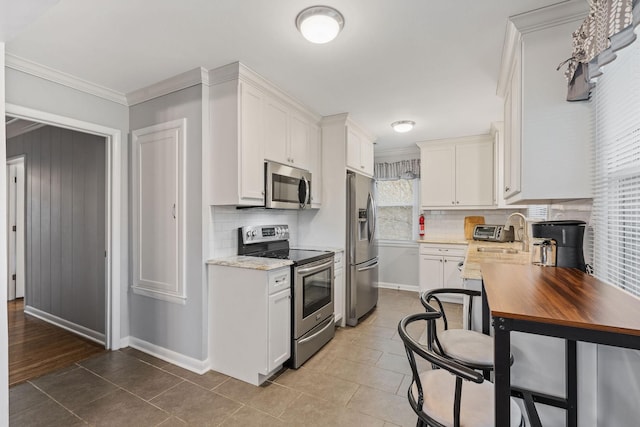 kitchen featuring light tile patterned floors, white cabinetry, ornamental molding, and appliances with stainless steel finishes