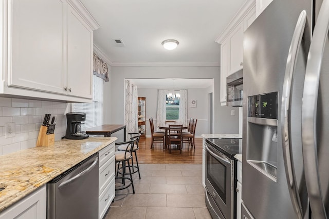 kitchen with white cabinets, crown molding, light stone countertops, light tile patterned floors, and appliances with stainless steel finishes