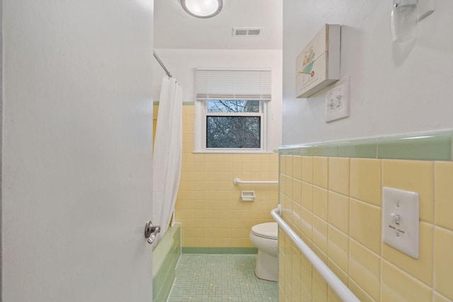 bathroom with tile patterned flooring, shower / tub combo, toilet, and tile walls