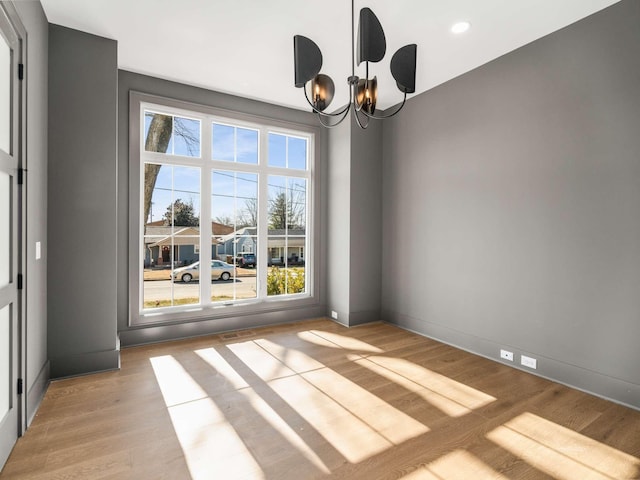 spare room featuring a notable chandelier and light wood-type flooring