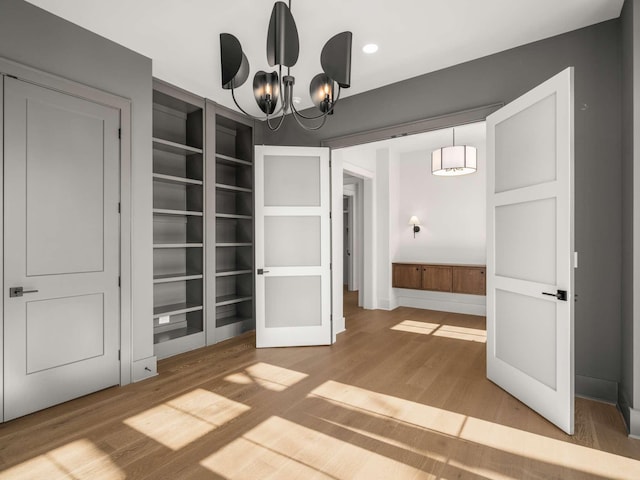 unfurnished dining area featuring an inviting chandelier, wood-type flooring, and built in features