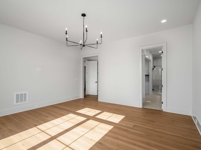 empty room with wood-type flooring and a notable chandelier